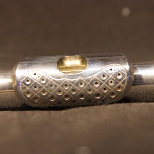 Detailed perspective of perforated lip plate with multiple circular holes on silver headjoint