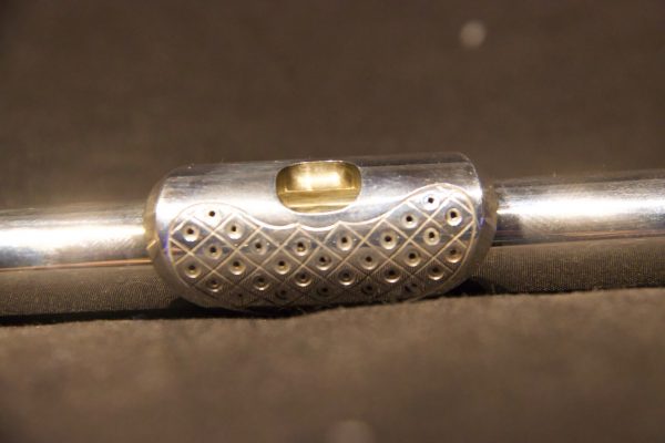 Detailed perspective of perforated lip plate with multiple circular holes on silver headjoint